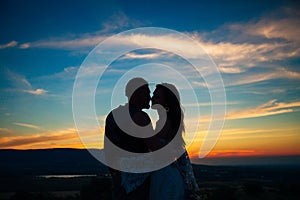 Silhouette of a couple hugging and kissing at sunset against the background of mountains and sea