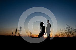 Silhouette of Couple hugging on Power lines background on sunset. Save the planet and electricity. Humanity and