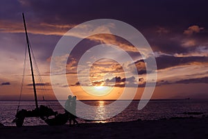 Silhouette couple kissing on the beach with catamaran sailboat.