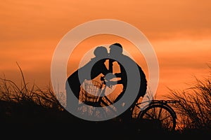 Silhouette couple kissing on bike over sunset background