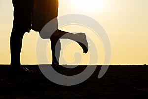 Couple kissing at sunset by the sea with one of her legs lifted up