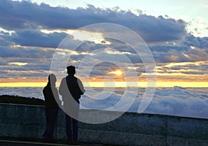 Silhouette couple looking at the beautiful sunrise on the top of