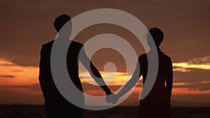 Silhouette couple in love. Male takes a female by the hand on background of golden sunset. Romantic couple in love at