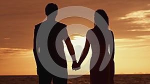 Silhouette of a couple in love standing together at sunset. Man touches her woman with his hand. Family at sunset on sea