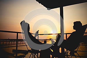 Silhouette of couple lover sitting and relax on romantic sunset at the sea of honeymoon vacation.