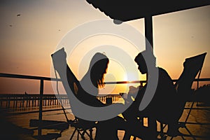 Silhouette of couple lover sitting and relax on romantic sunset at the sea of honeymoon vacation.