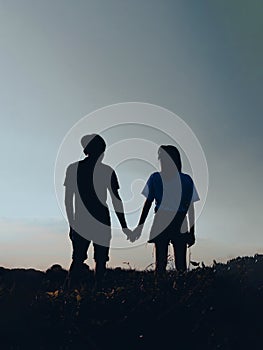 Silhouette couple man and women holding hand and walking together under sunset sky