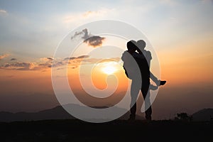 Silhouette of a couple on the mountain, A young romantic couple enjoy a beautiful view of the sun setting over the mountains, love