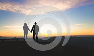 Silhouette of a couple on the mountain, A young romantic couple enjoy a beautiful view of the sun setting over the mountains, love