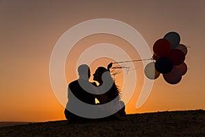 Silhouette of a couple playing with balloons at sunset