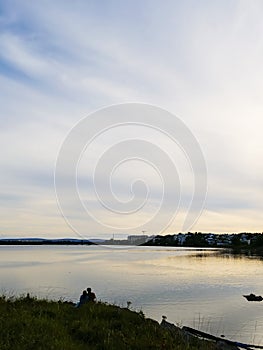 Silhouette of a couple sitting by a lake. Town buildings in the background. Romantic scene with a man and a woman. Love and