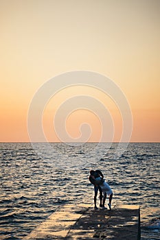 Silhouette of couple standing and kissing at the pier, watching the sunrise at the beach summer time