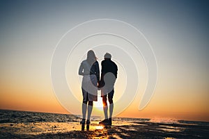 Silhouette of couple standing at the pier, watching the sunrise at the beach summer time