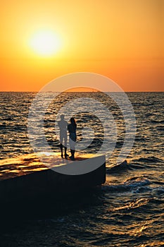 Silhouette of couple standing at the pier, watching the sunrise at the beach summer time