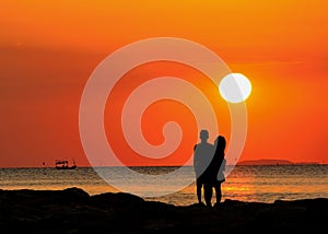 Silhouette of couple standing by the sea watching the sunset.
