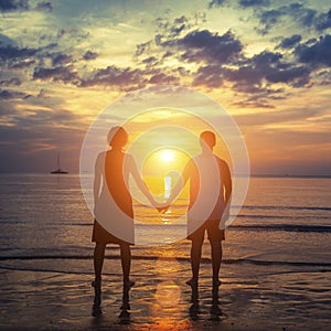 Silhouette of a couple on their honeymoon standing on the ocean beach at amazing sunset.