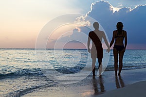 Silhouette Of Couple Walking Along Beach At Sunset