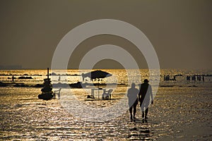 Silhouette with couple walking on beach, shiny sea water and other people, Kihim beach, Alibag