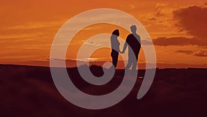 Silhouette of couple walking on beach at sunset holding hands. happy man and girl on seashore in the lights of sunset