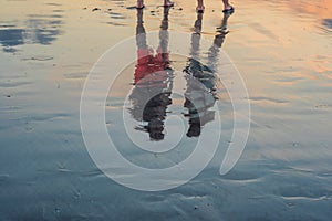 Silhouette of couple walking and talking on beach with drop shadow reflected on calm sea water surface in evening sunset. Holiday