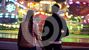 Silhouette of couple, which standing back to camera and watching rotation of attractions in amusement park. Lovers