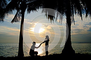 Silhouette couple, woman stand and man sit on the floor and hold her hand for propose her to wedding