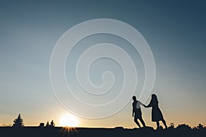 Silhouette of couples who holding hands climbs the hill