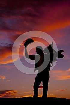 Silhouette of a cowboy holding his hat up and a saddle on should