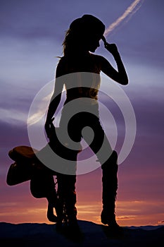 Silhouette of a cowgirl hold saddle in hand hold hat