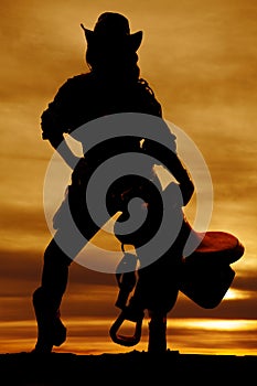 Silhouette of cowgirl holding saddle straight on