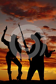 Silhouette of cowgirl holding up gun in the air