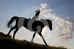 Silhouette of cowgirl riding horse through the dusk prairie