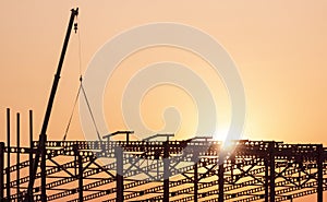 Silhouette crane lifting castellated beam to installing on large industrial building structure in construction site at sunset