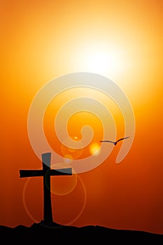 Silhouette of the cross and bird with the sunset flare.