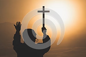 Silhouette the cross in hands, religion symbol in light and landscape over a sunrise, background, religious, faith concept