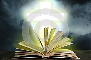 Silhouette of cross and open Bible on grey table against cloudy sky