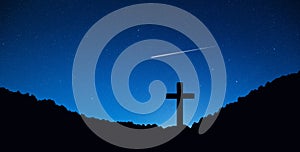 Silhouette of crucifix cross on mountain at night time with star and space background.