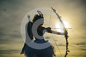 Silhouette of a cupid. Side view of teen girl archer against sunset. Happy Valentines day.