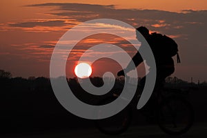 The silhouette of a cyclist against the background of the sun and the beautiful sky. The outline of a man riding on a bicycle