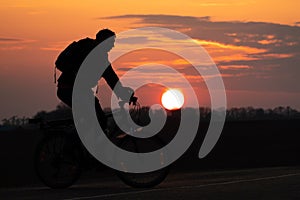 The silhouette of a cyclist against the background of the sun and the beautiful sky. The outline of a man riding on a bicycle