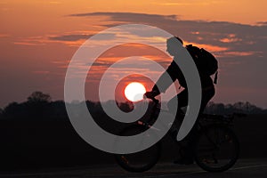 The silhouette of a cyclist against the background of the sun and the beautiful sky. The outline of a man riding on a bicycle