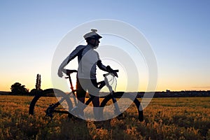 Silhouette of a cyclist with a Bicycle in a field at sunset