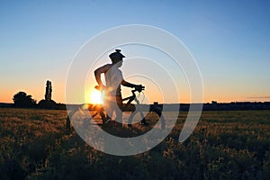 Silhouette of a cyclist with a Bicycle in a field at sunset