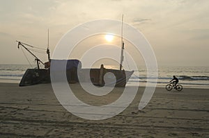 Silhouette of a cyclist passing by a ship wreak on sunset beach photo
