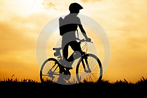 Silhouette of cyclist riding a road bike at at sunset with orange sky in countryside.