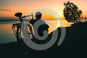 Silhouette of cyclist traveler with his bicycle enjoy sunset view together by tranquil Sevan lake in nature. Bicycle touring