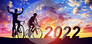 Silhouette of cyclists with bicycles at sunset. New Year 2022 concept.