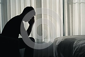 Silhouette depressed man sadly sitting on the bed in the bedroom