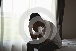 Silhouette depressed man sadly sitting on the bed in the bedroom. Sad asian men suffering depression insomnia awake and sit alone