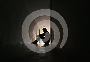 Silhouette of depressed man sitting on walkway of residence building.